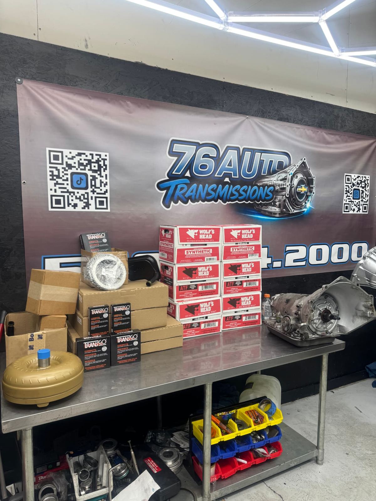 Transmission rebuild parts staged on the 76Auto workbench: clutch packs, kits and a torque converter